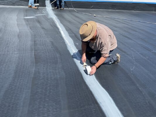 Worker applying seam tape on a flat commercial roof