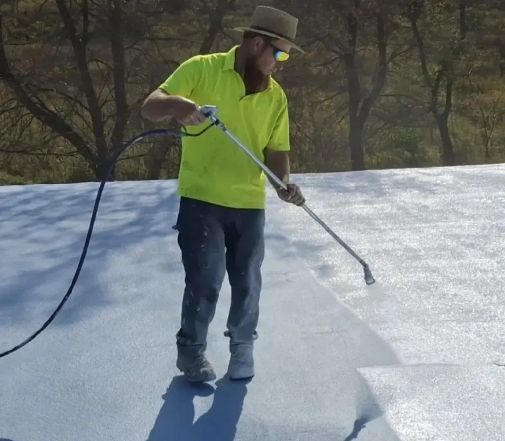 Worker in neon shirt spraying white coating on flat roof